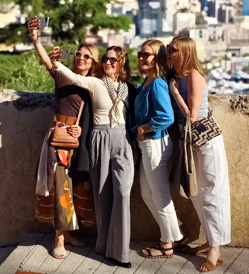 Cztery uczestniczki wyjazdu CoolTurystek robią selfie przy kamiennym murku, z portem w tle.