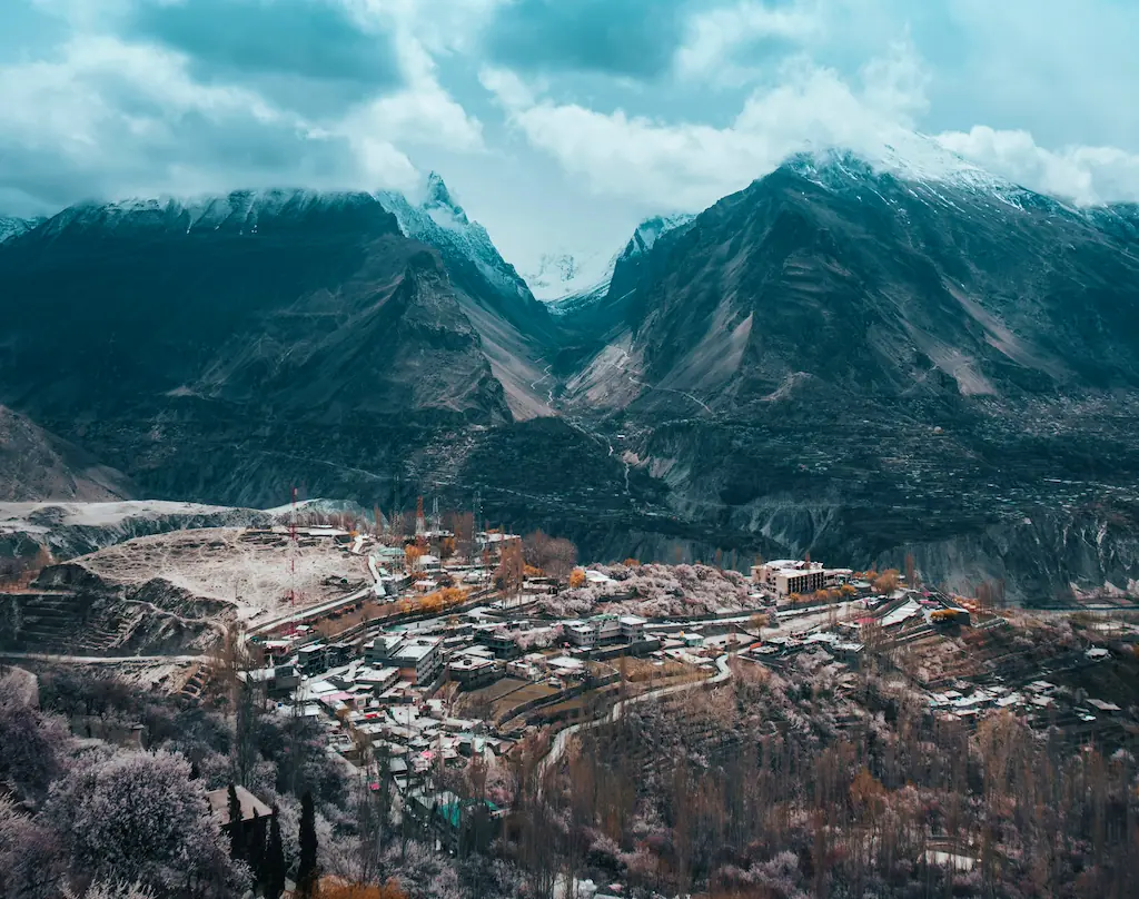 Zabudowania i tarasowe pola wśród kwitnących drzew na zboczu doliny Hunza, pod górami ze śniegiem i niskimi chmurami