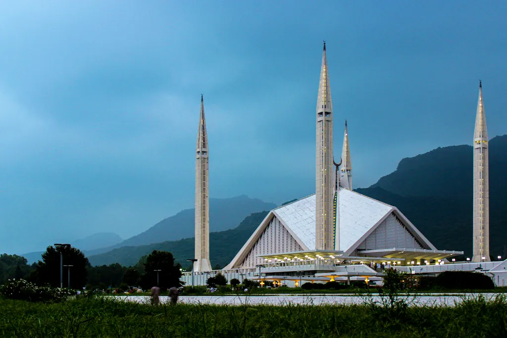 Biały meczet Faisal z wysokimi minaretami na tle ciemnych wzgórz i zachmurzonego nieba w Islamabadzie