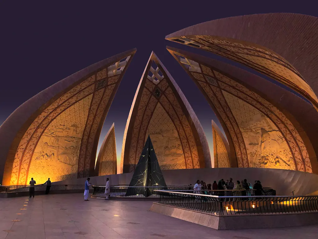 Podświetlone płatki Pakistan Monument z reliefami i zwiedzającymi przy balustradzie w Islamabadzie po zmroku