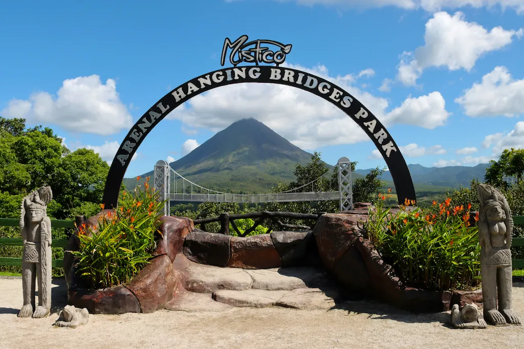 Brama parku Mistico z napisem Arenal Hanging Bridges Park i wulkanem Arenal w tle