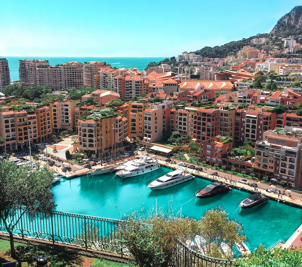 Port Fontvieille w Monako z jachtami na turkusowej wodzie i różową zabudową wokół nabrzeża.