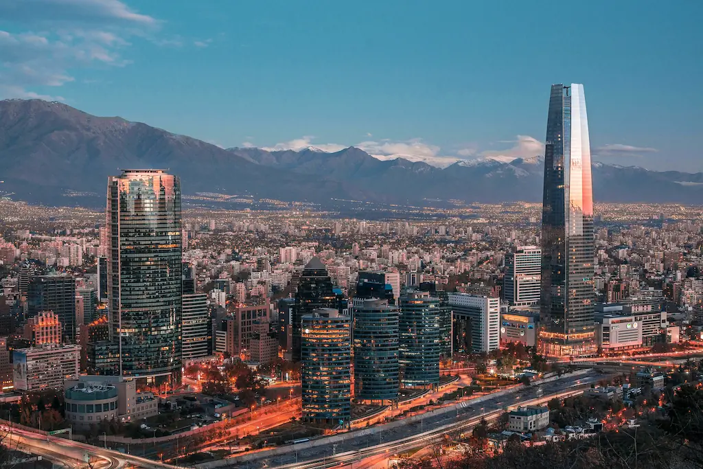 Santiago de Chile u podnóża Andów Panorama Santiago de Chile z wieżowcem Gran Torre Santiago, Andami i rozświetlonymi ulicami o zmierzchu