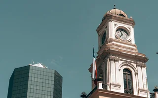 Architektura podczas zwiedzania Santiago de Chile Zabytkowa wieża zegarowa w Santiago z kopułą i chilijską flagą, obok nowoczesnego szklanego budynku