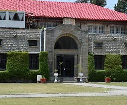 Kamienna fasada Taxila Museum z łukowym wejściem, czerwonym dachem i zielenią